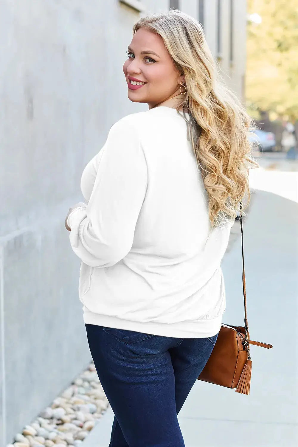 Plus size woman in a white V-neck lantern sleeve top and dark wash jeans.