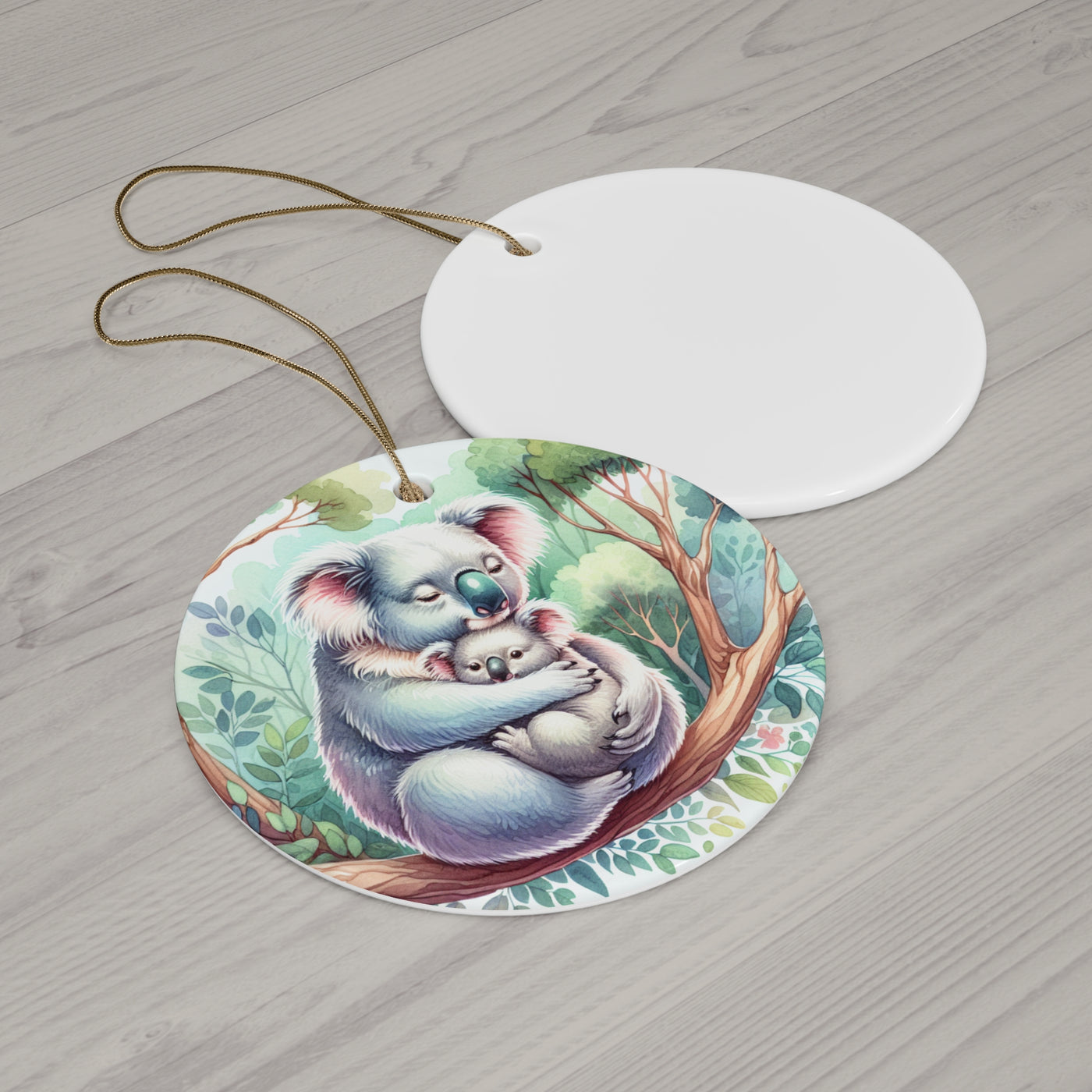 A round ceramic ornament with a watercolor painting of a mother koala hugging her baby.