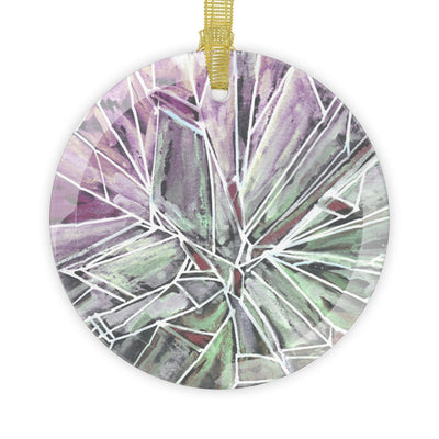 A round glass ornament with a green and purple "break the glass" design and a gold ribbon.