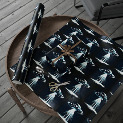 UFO-themed wrapping paper with a gift, scissors, and tape on a wooden table.
