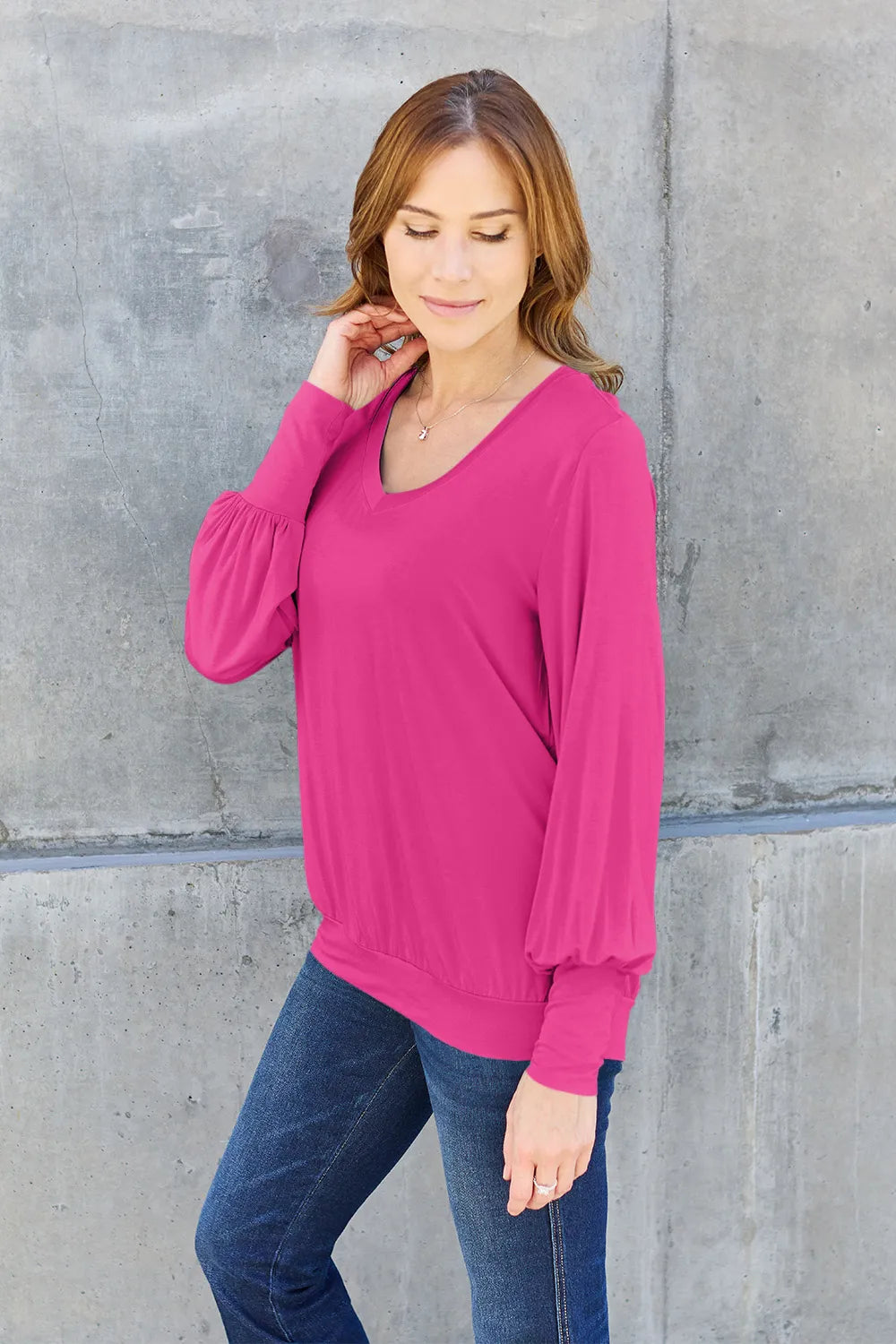 A woman wears a bright pink V-neck top with lantern sleeves and dark wash jeans.
