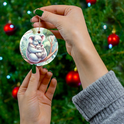 A ceramic ornament with a koala and joey on a branch, held by hands.