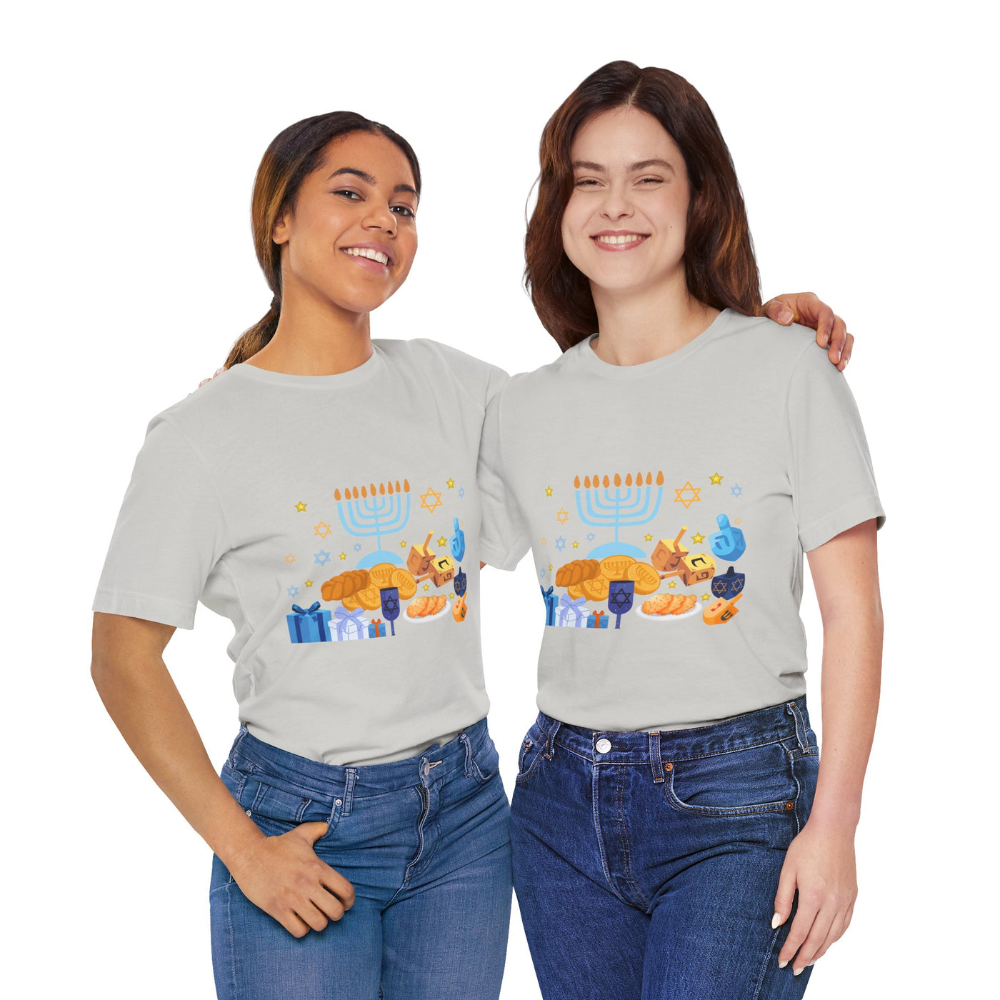 Two women in light grey t-shirts with a Hanukkah graphic print stand with arms around each other.