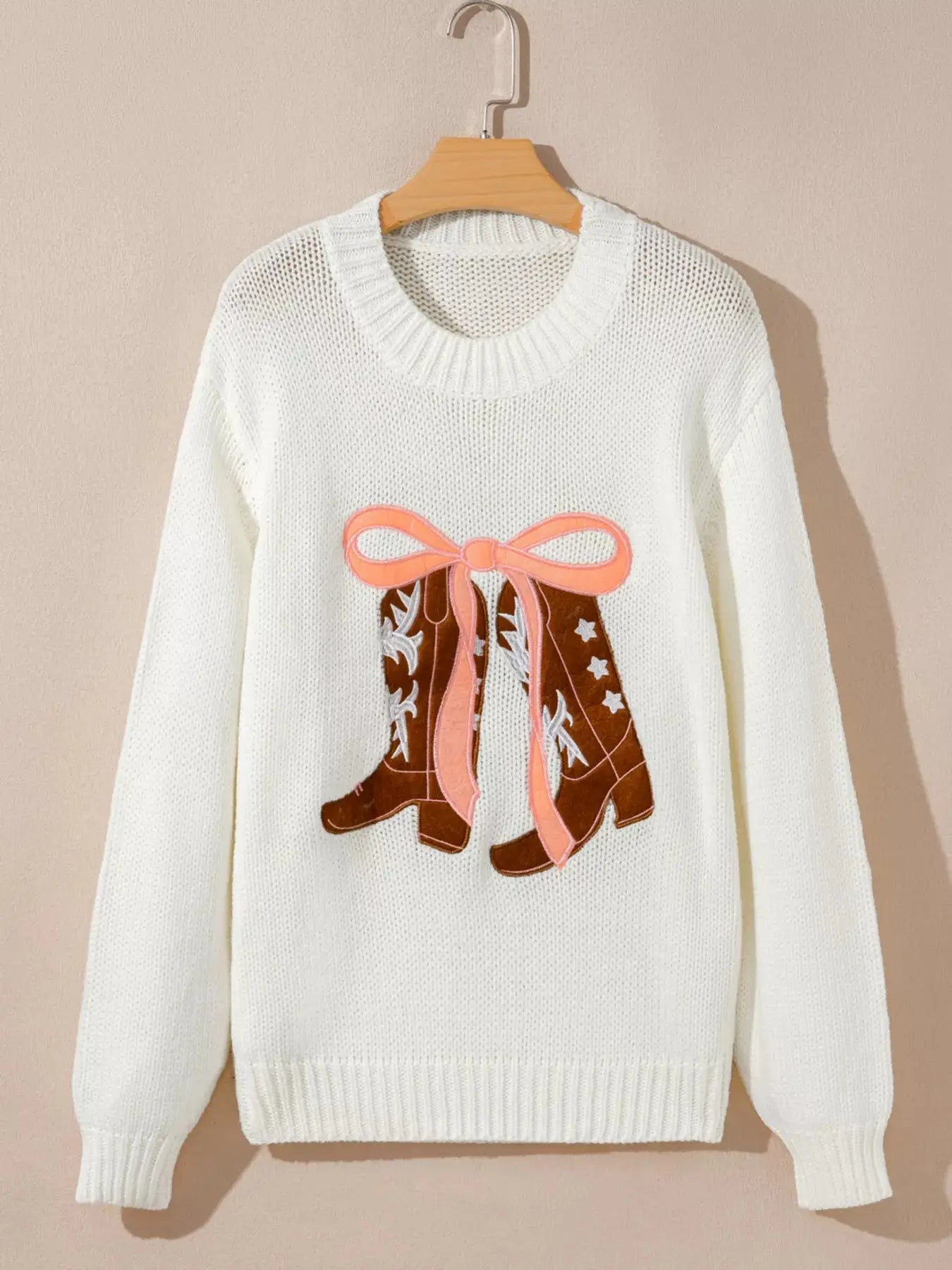 White knit sweater with embroidered cowboy boots and a pink bow.