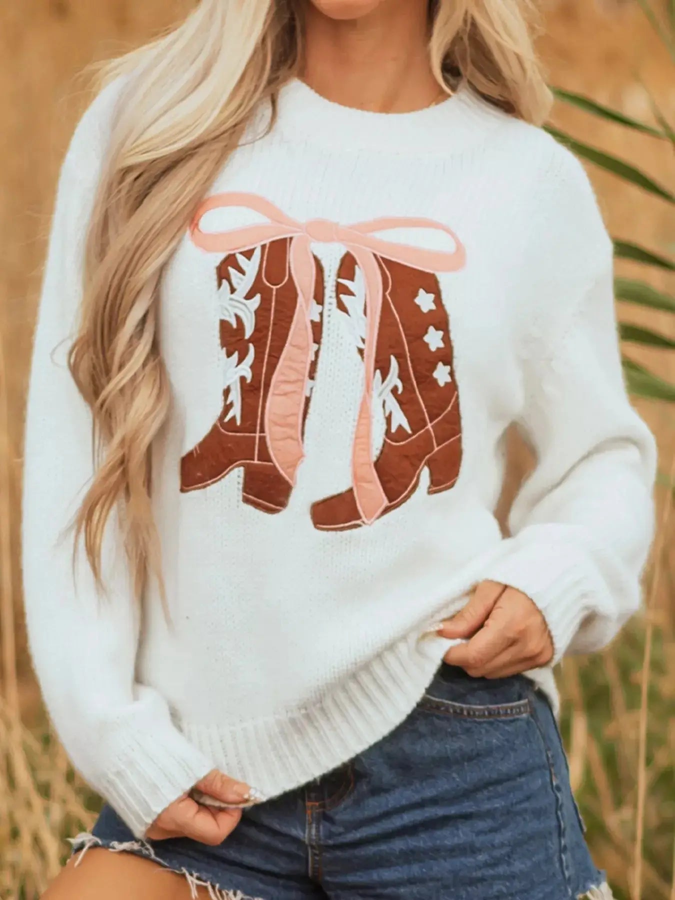 White drop shoulder sweater with embroidered cowboy boots and pink bow detail.