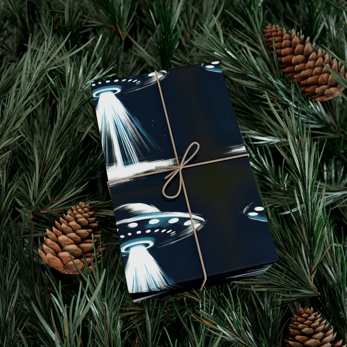 UFO design wrapping paper tied with twine, surrounded by pine needles and pinecones.