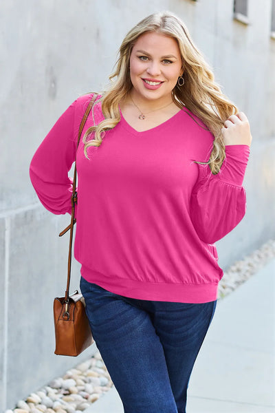A woman wears a bright pink V-neck top with lantern sleeves and dark wash jeans.