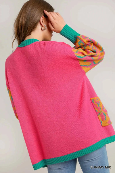 Pink oversized cardigan with green trim and patterned sleeves and pockets.