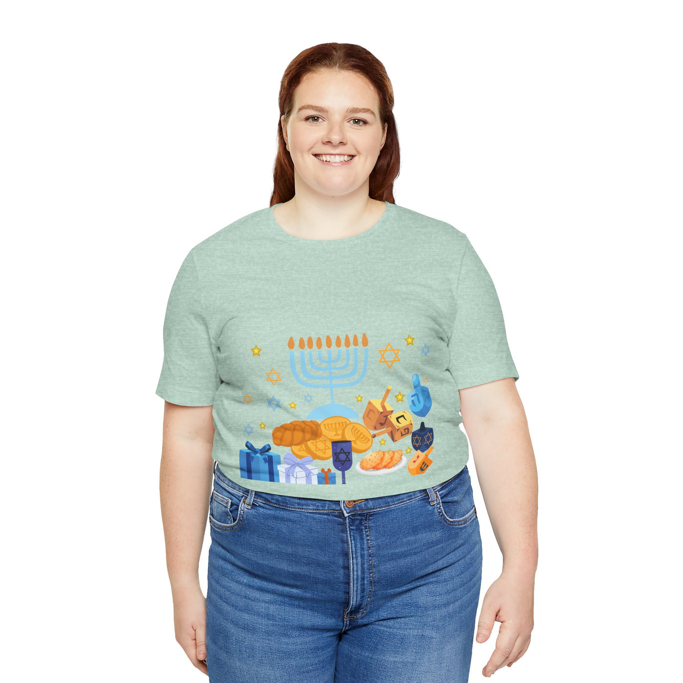 A woman wears a light green t-shirt with a Hanukkah graphic featuring a menorah, dreidels, gelt, and gifts.