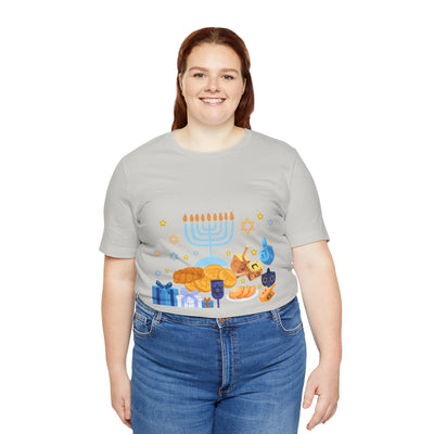 A woman wears a light grey t-shirt with a graphic of a menorah, dreidels, gelt, and gifts.