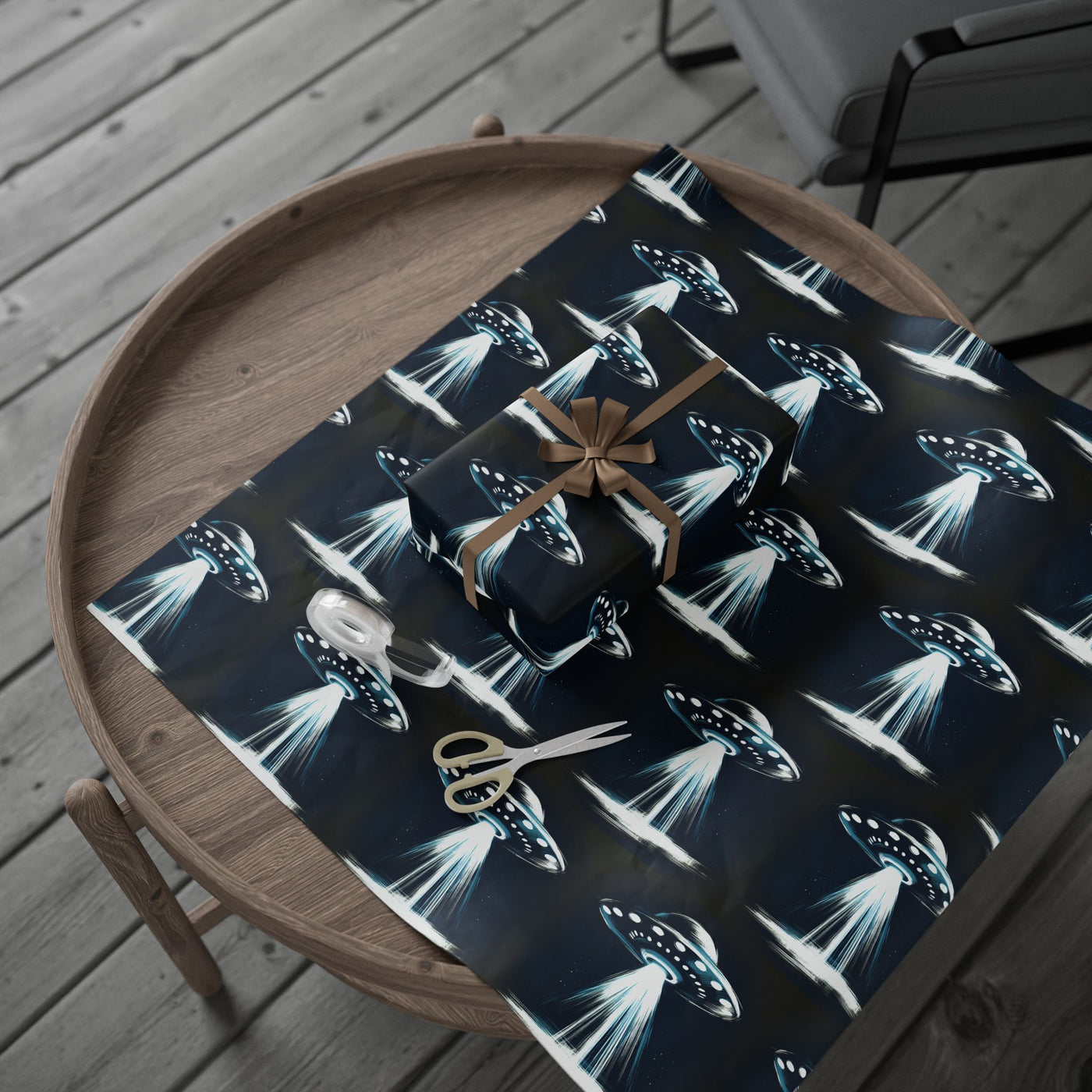 UFO-themed wrapping paper with a gift, ribbon, and scissors on a wooden table.