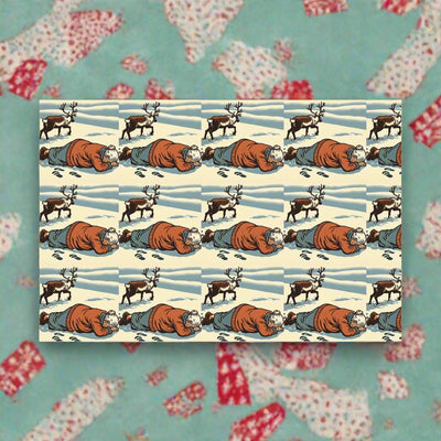 Wrapping paper with a repeating pattern of a person lying in the snow with reindeer.
