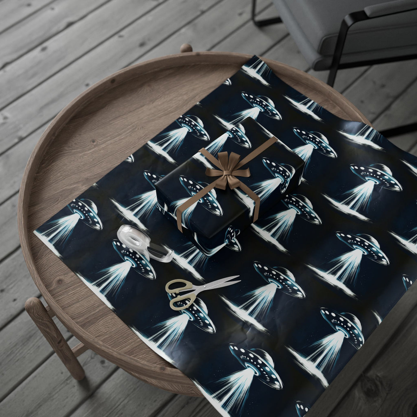 UFO-themed wrapping paper with a gift, ribbon, tape, and scissors on a wooden table.