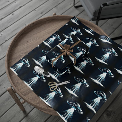 UFO-themed wrapping paper with a gift, ribbon, tape, and scissors on a wooden table.