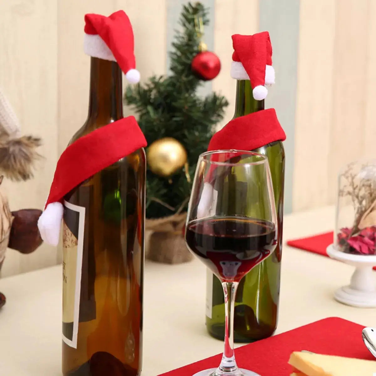 Two wine bottles are decorated with red Santa hats and scarves.