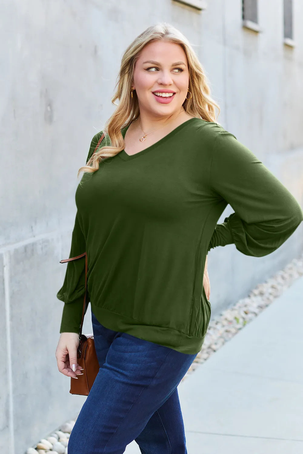 A woman wears a green V-neck top with lantern sleeves and dark wash jeans.