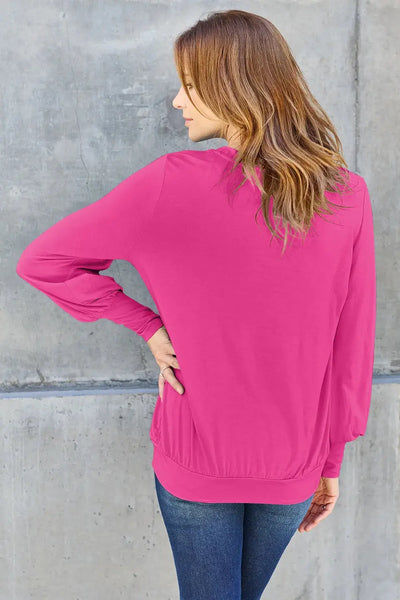 A woman wears a bright pink V-neck top with lantern sleeves.