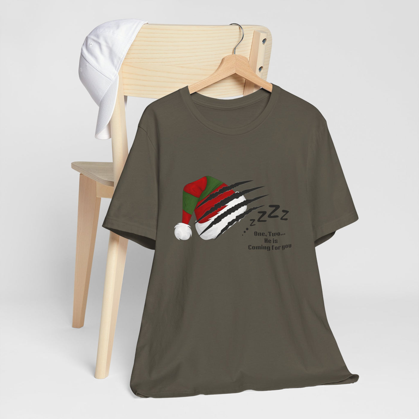A dark grey t-shirt with a graphic of a Santa hat being clawed, with "Zzz" and "One, Two... He is Coming For You" text.