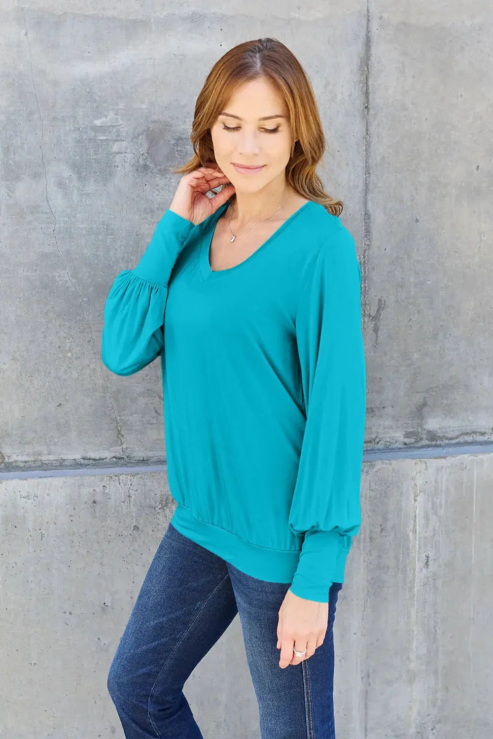A woman wears a teal v-neck top with lantern sleeves and dark wash jeans.