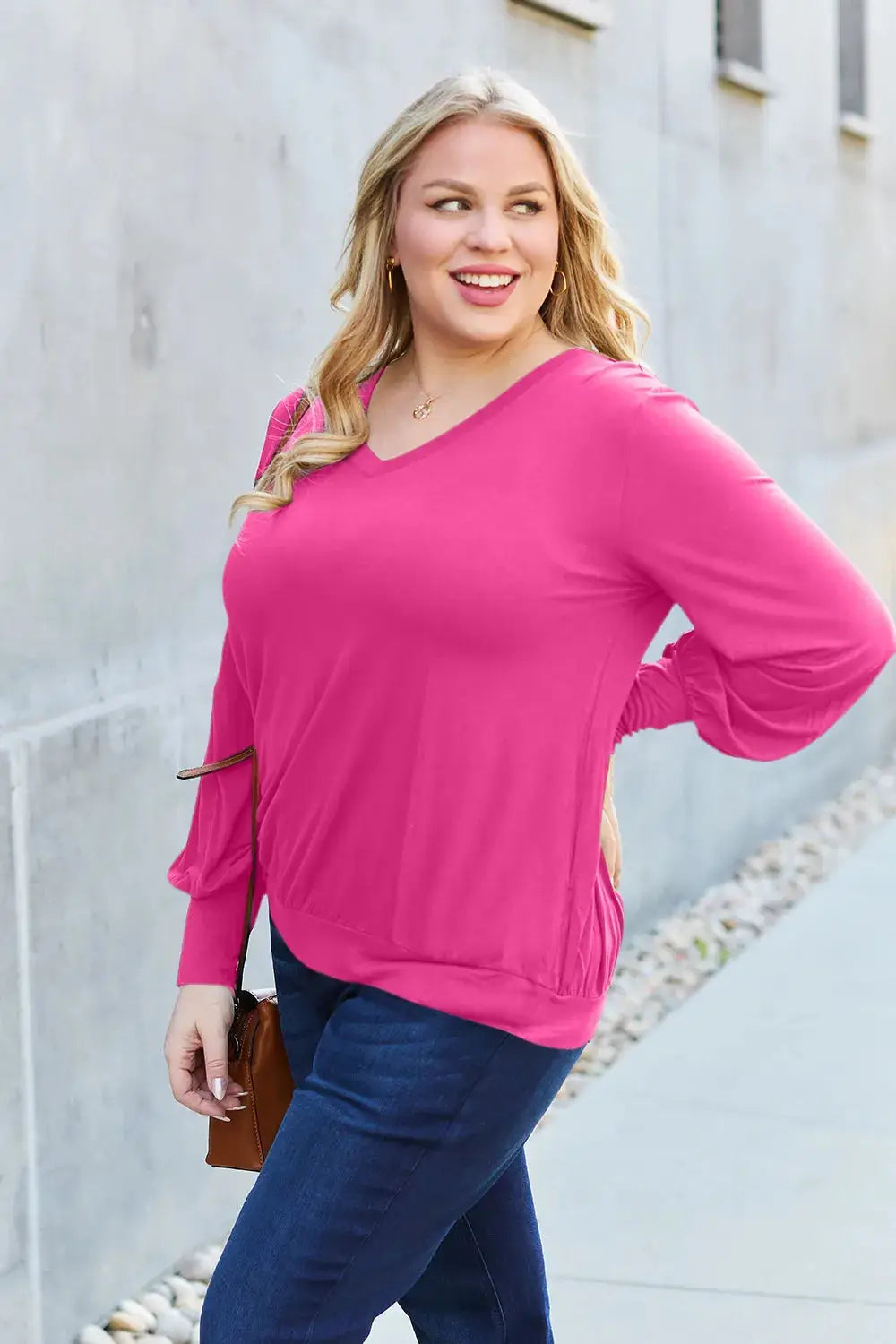 A woman wears a bright pink V-neck top with lantern sleeves and dark wash jeans.