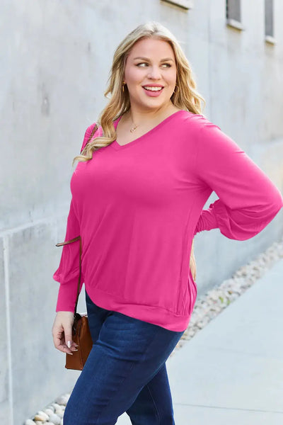 A woman wears a bright pink V-neck top with lantern sleeves and dark wash jeans.