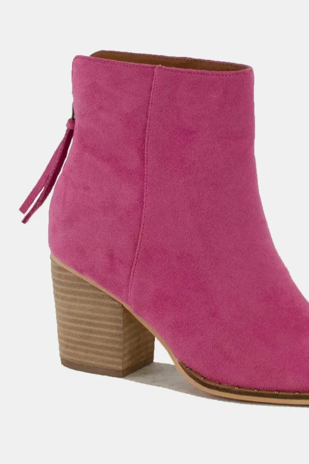 A pink suede ankle boot with a wooden block heel and a tassel detail.
