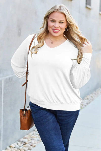 A woman wears a white v-neck lantern sleeve top and blue jeans.