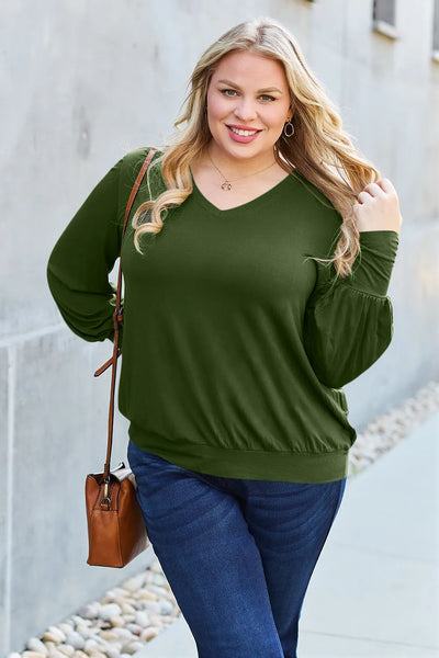 A woman wears a green V-neck top with lantern sleeves and blue jeans.