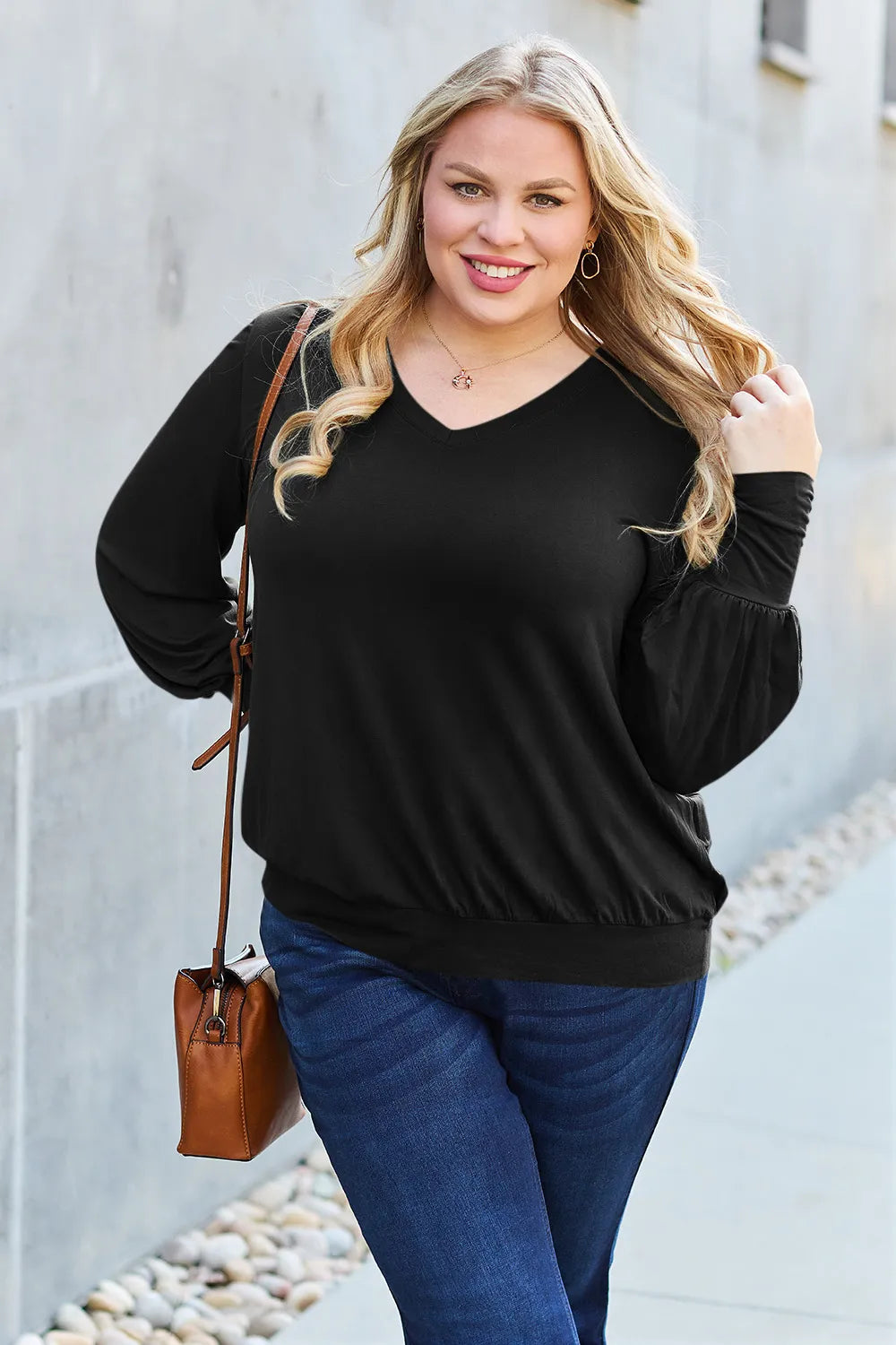 A woman wears a black V-neck top with lantern sleeves and blue jeans.